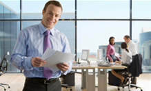 Smiling businessman holding paperwork with co-workers working in background